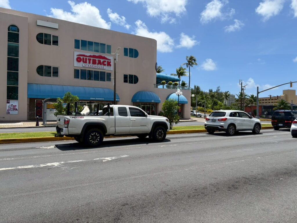 グアムのタモン地区にあるアウトバック・ステーキハウスが入る商業施設と通りを走る白いピックアップトラック