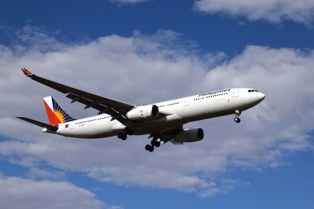 青空と白い雲の中を飛行する、フィリピン航空のエアバスA330の全景。