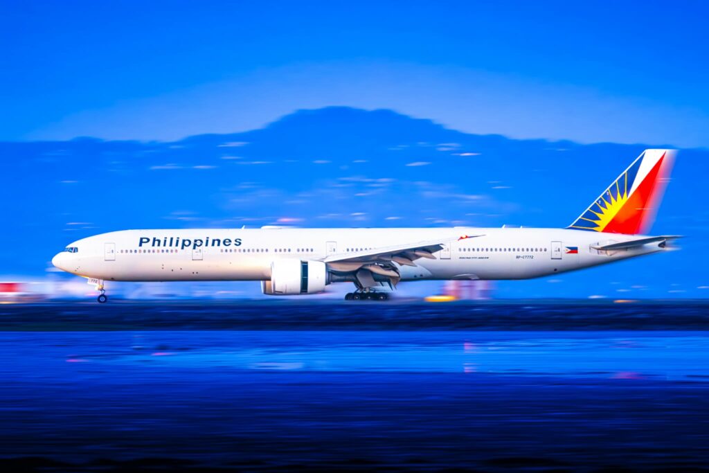 夕暮れ時の滑走路を高速で走行し、背景に山々が広がるフィリピン航空のボーイング777。