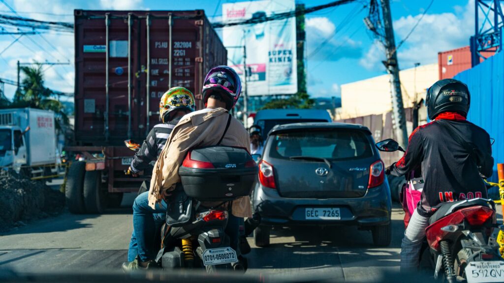 セブ島の道路で大型コンテナ車の横を走る、ヘルメットを被った二人乗りのバイク。