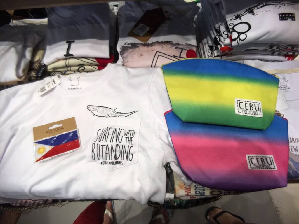 セブ島のお土産雑貨。ジンベエザメが描かれた白いTシャツと、フィリピン国旗のワッペン、カラフルな「CEBU」ロゴ入りポーチ。