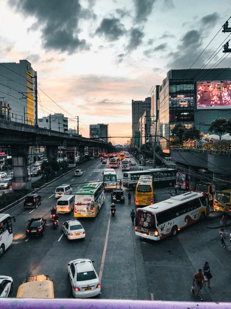 マニラの夕暮れ時、高架鉄道（LRT/MRT）沿いの幹線道路（EDSA）を埋め尽くすバスや車、バイクの列と都会の夜景