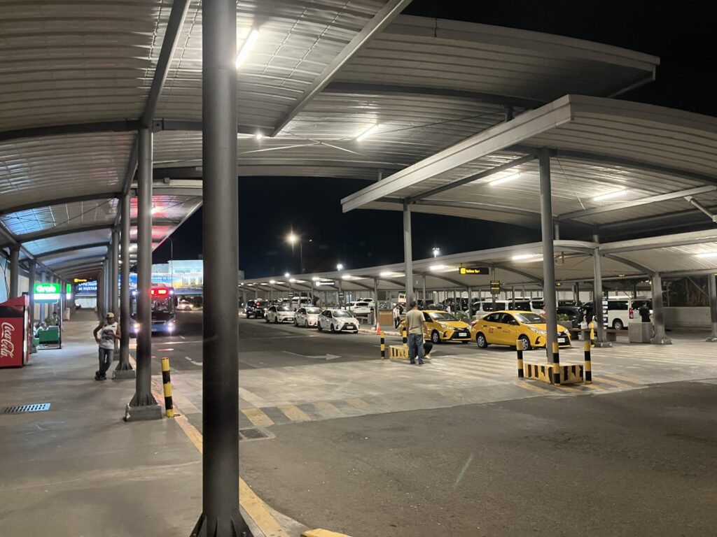 夜のマクタン・セブ空港の到着階。屋根付きの車寄せに黄色いタクシーが並び、奥にGrabの看板が見える